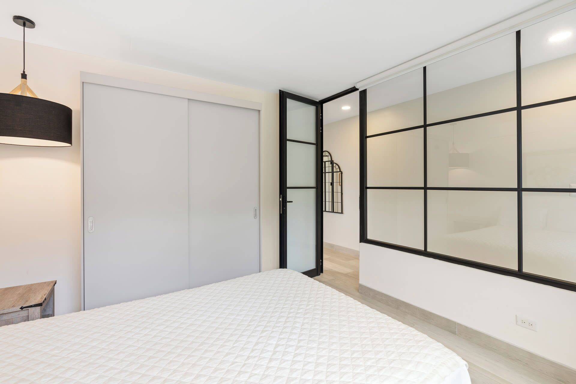 A bedroom with a bed, a wardrobe, a hanging light fixture, and a sliding glass door leading to another room.