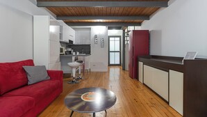 Ett kompakt bostadsutrymme med ett litet pentry, en röd soffa, en vinylskiva på ett litet bord och ett träpanelat tak.