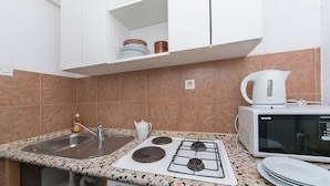 A kitchen with a sink, stove, microwave, and shelves above the counter. - Enchanting apartment with WiFi in beautiful Brela with a loggia (Brela)