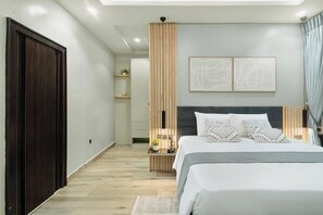 A modern bedroom with a large bed, bedside tables, a wooden partition, and abstract wall art. - Kashco Apartments (Abuja)