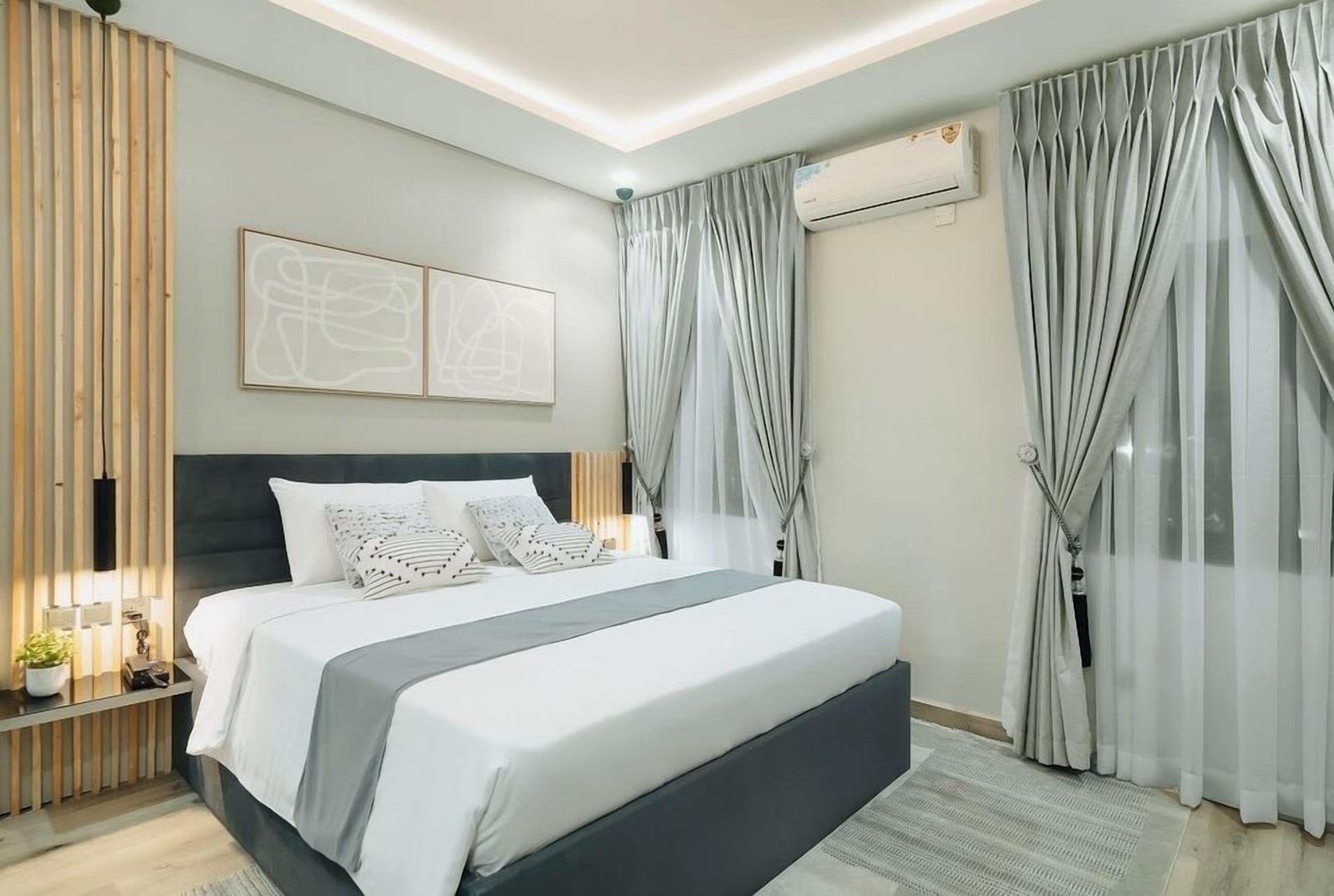 Une chambre moderne avec un grand lit, une table de chevet avec une lampe et un climatiseur fixé au mur.