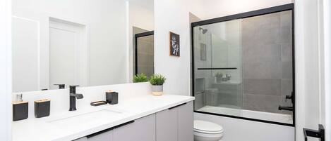 Un baño moderno con tocador blanco, un espejo grande, cabina de ducha con paredes de vidrio y un inodoro.
