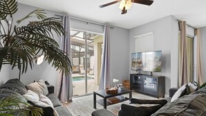 A modern living room with a sofa, coffee table, and television. There is a large plant and a ceiling fan. - Disney Getaway! Townhouse with Private Pool. Book Now! #SLR476 (Orlando)