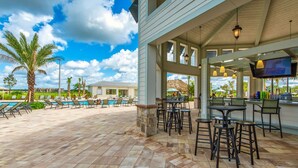 An outdoor patio area with poolside chairs, a bar with stools, and a television screen. - Disney Getaway! Townhouse with Private Pool. Book Now! #SLR476 (Orlando)