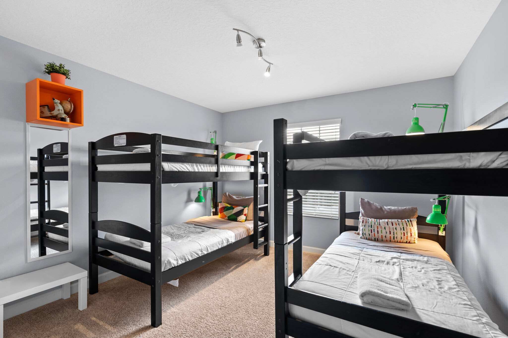 Een slaapkamer met een stapelbed, een bureau, een plank met een plant en een raam met jaloezieën.