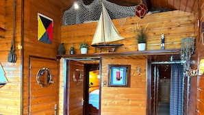 Interior de una cabaña de madera con temática náutica, que incluye un modelo de velero, una bandera y una red colgada del techo.