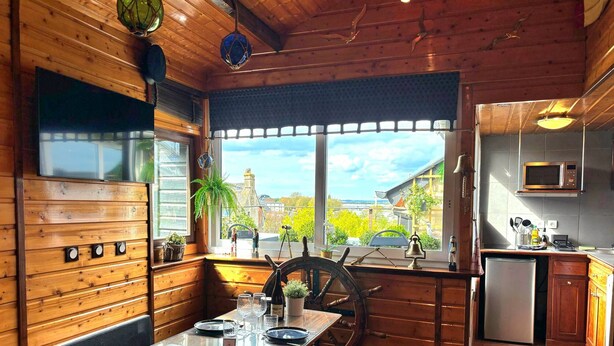 Un interior de madera con comedor, vistas a través de una ventana y una cocina con microondas.