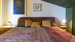 Une chambre avec un grand lit, deux tables de chevet, un tableau encadré au-dessus du lit et un plafond en bois.