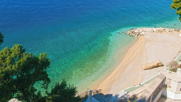 Une vue sur la côte, avec une eau turquoise cristalline, une plage de sable et un promontoire rocheux.