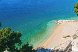 A coastal view with clear turquoise waters, a sandy beach, and a rocky outcrop.
