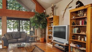 Un salon chaleureux avec un canapé, une table basse, un téléviseur et des étagères en bois remplies de livres et d’objets décoratifs.