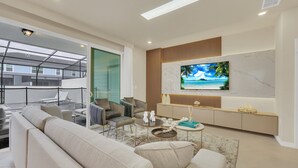 Un soggiorno moderno con un'ampia TV a schermo piatto, posti a sedere confortevoli e una porta vetrata che dà su un balcone esterno.