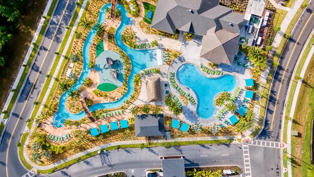 An aerial view of a resort with multiple swimming pools, a road, and surrounding greenery.