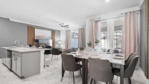 A modern kitchen with a central island, dining area with a table set for four, and a large window with curtains.
