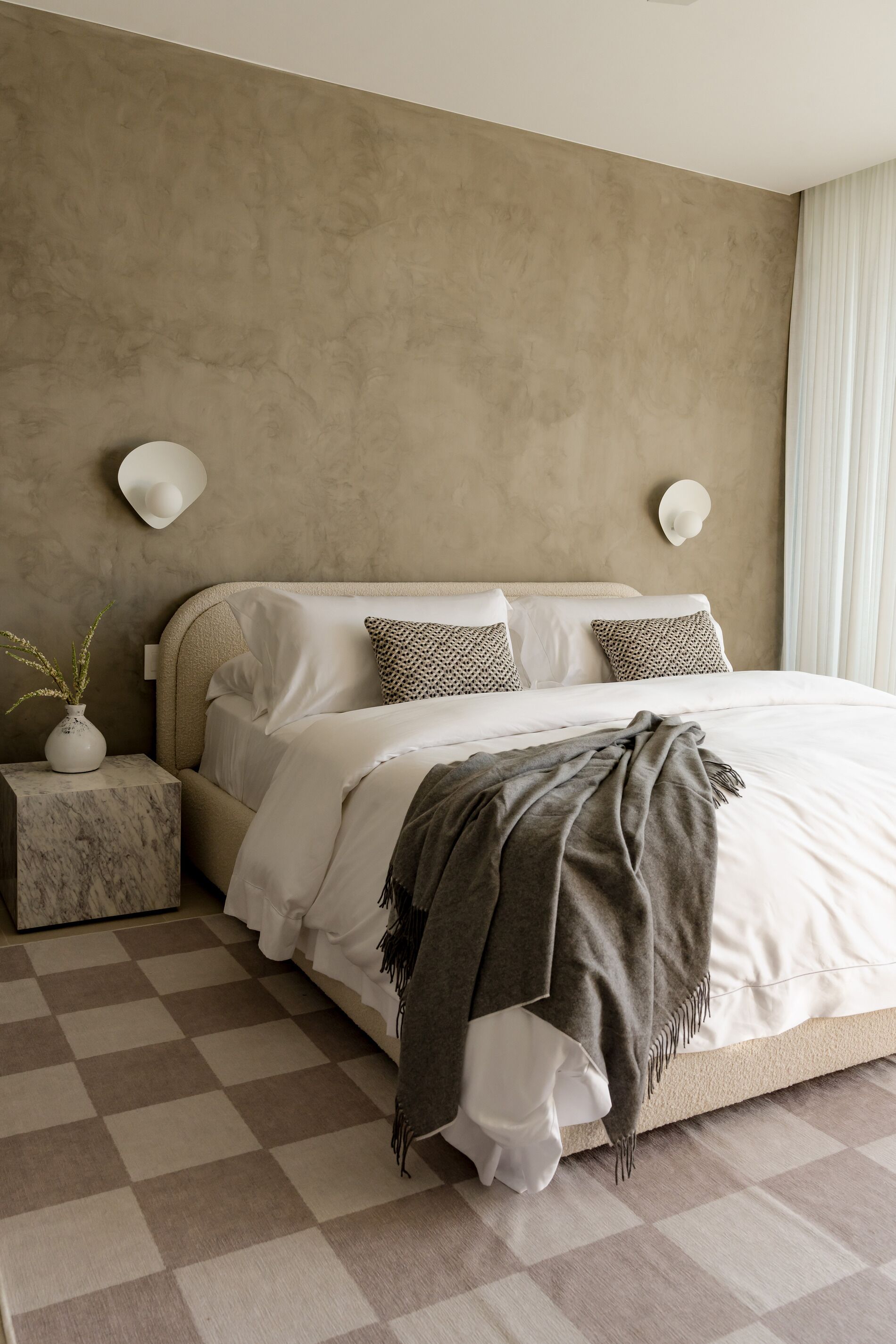 Ein Schlafzimmer mit einem großen Bett, einem мраморный Nachttisch, einer Vase mit Pflanzen und einem karierten Boden.