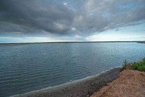 A calm body of water with a rocky shoreline and a distant landmass under a cloudy sky.