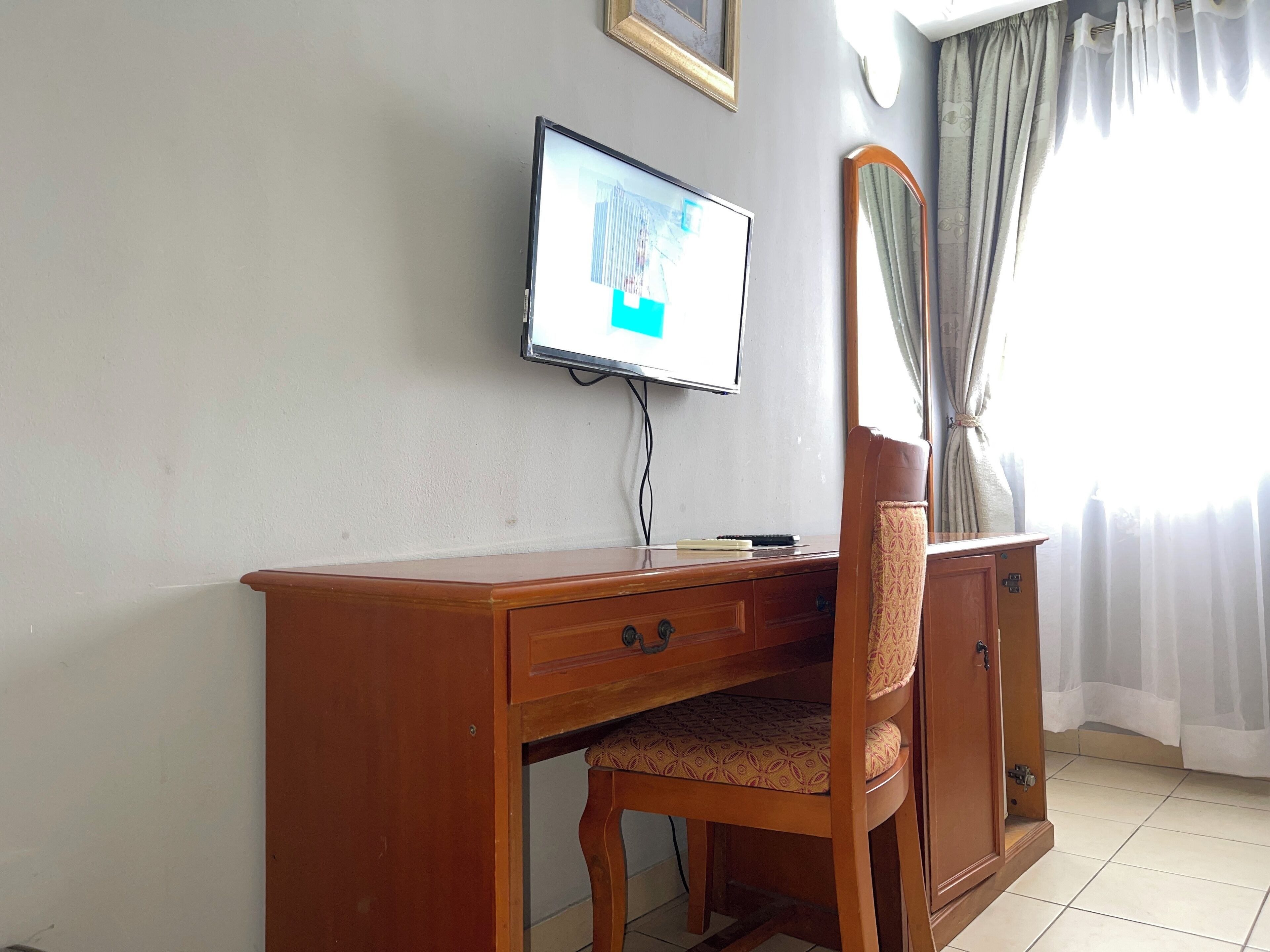 A wooden desk with a chair, a television mounted on the wall, and a window with curtains.
