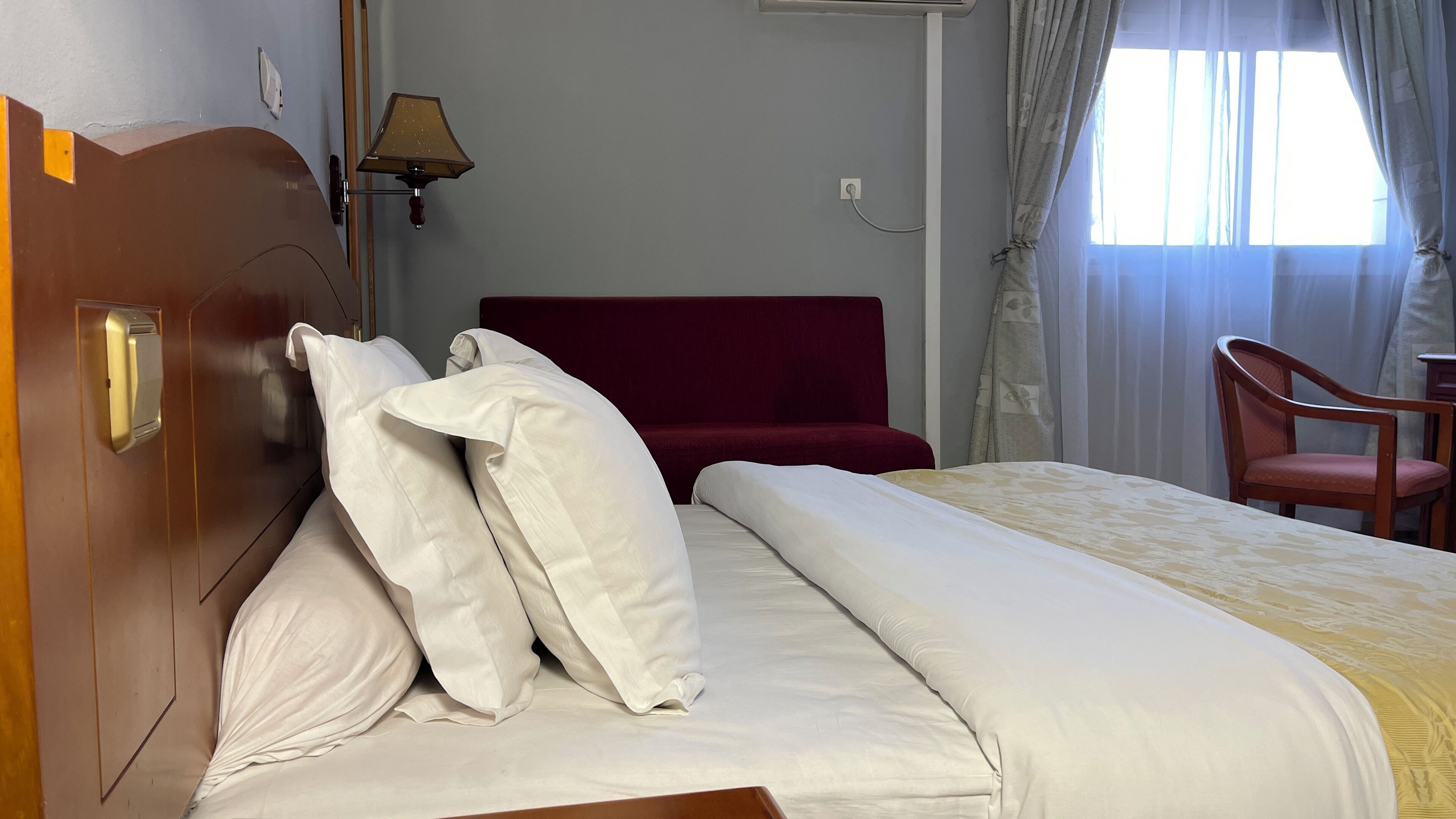 Ein Hotelzimmer mit einem Bett, einem roten Sofa, einem Holzstuhl und einer Lampe.