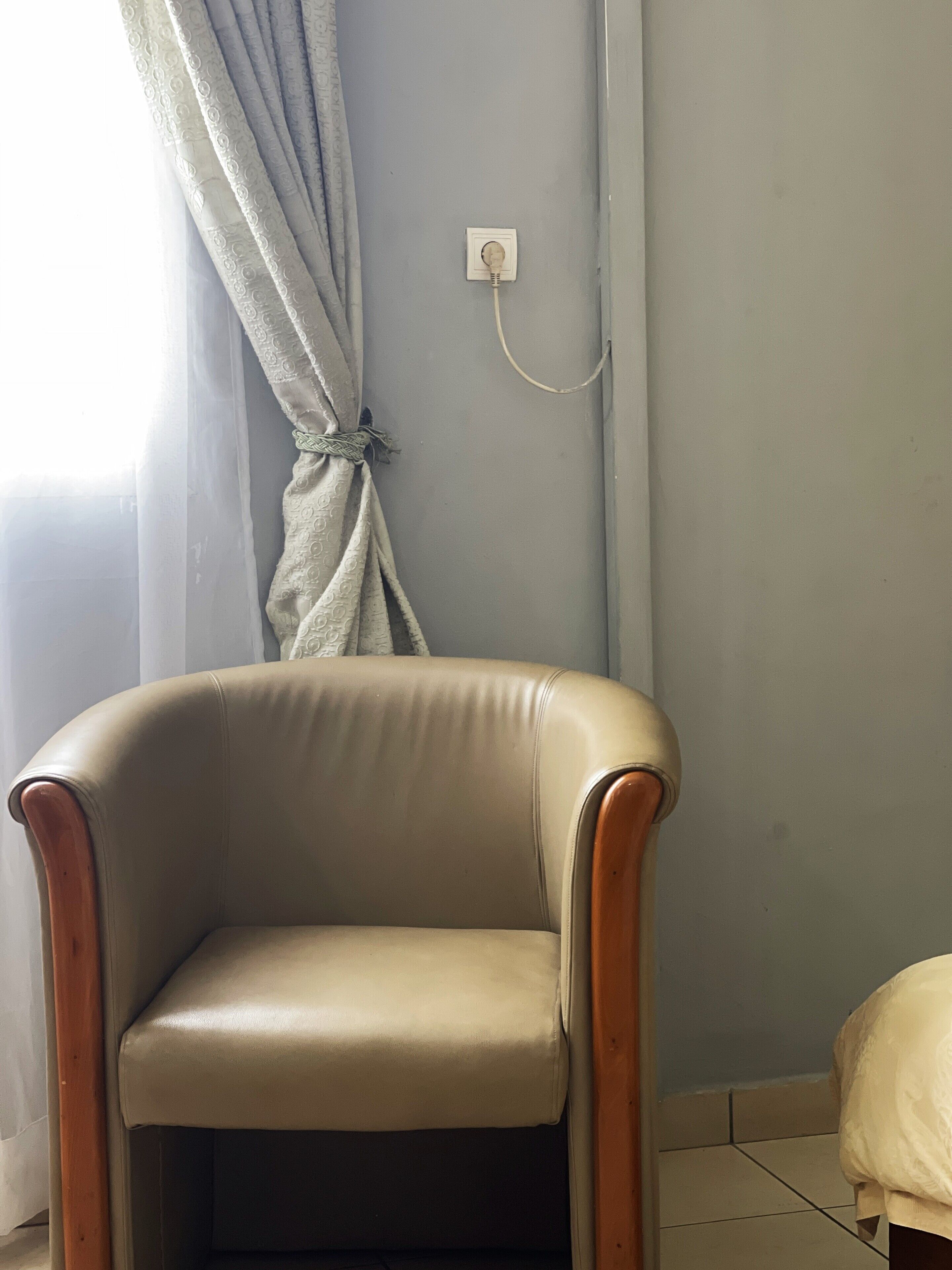 Une chaise avec un cadre en bois et un siège rembourré, placée dans une pièce dont le mur est d’un bleu clair et qui est équipée d’une prise de courant.