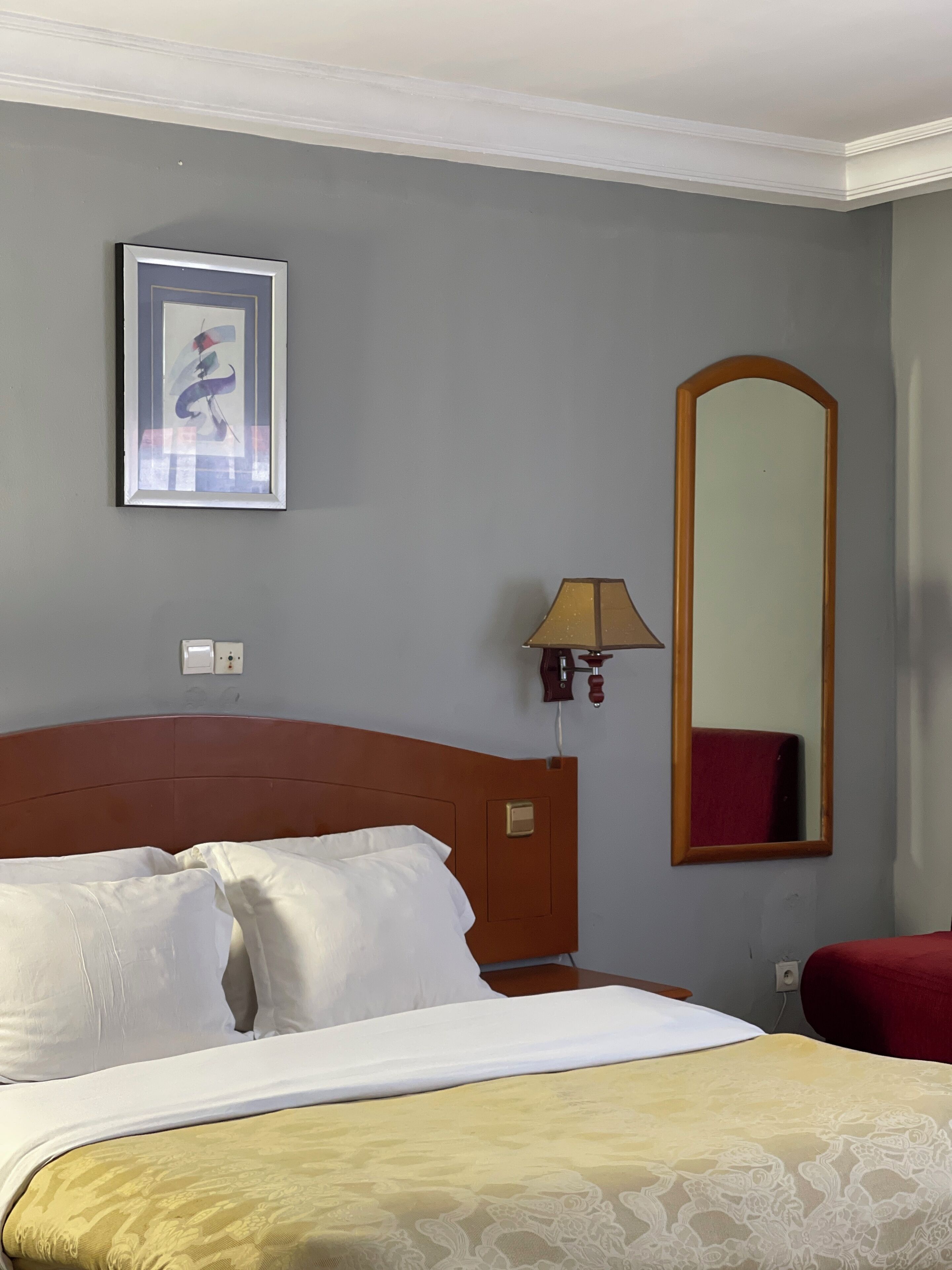 A hotel room with a bed, a framed picture on the wall, a mirror, and a lamp.