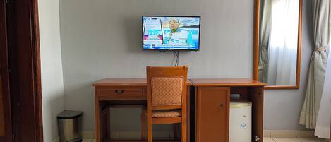 A room with a wooden desk, chair, and a television mounted on the wall.