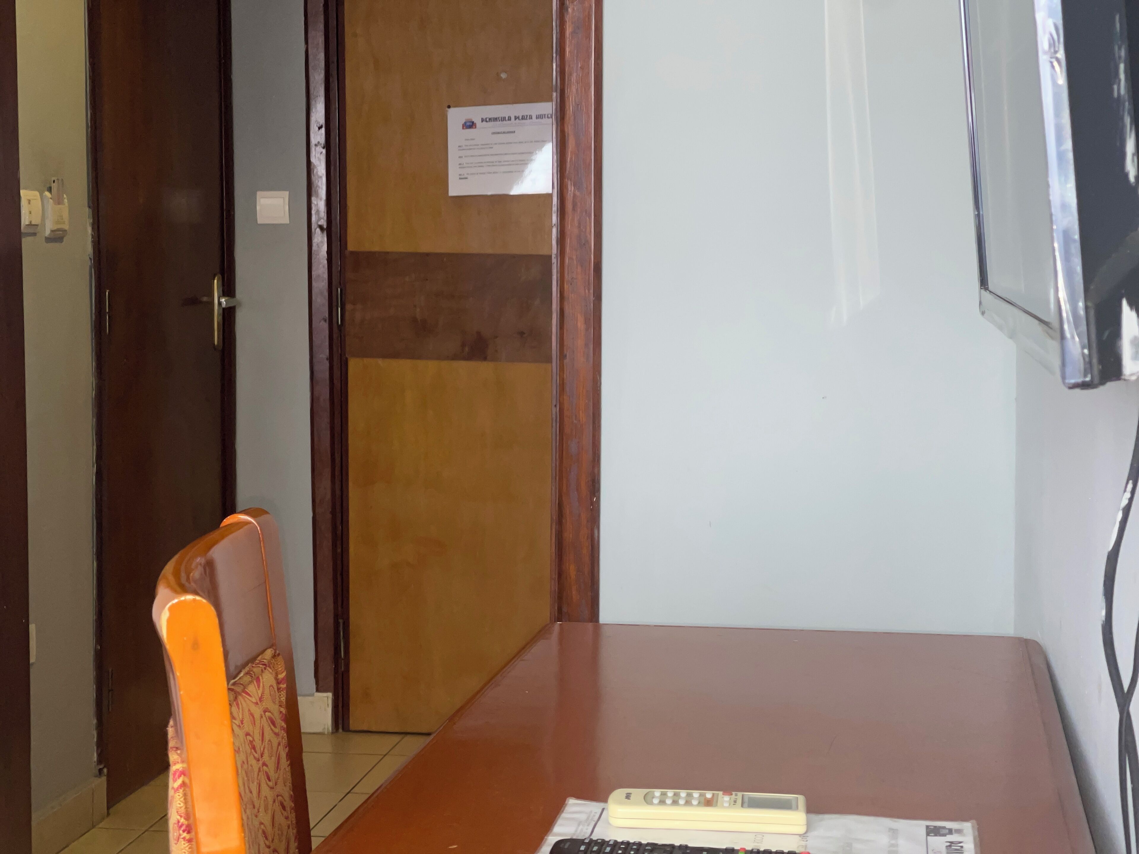 A hotel room with a wooden door, a desk with a telephone, and a sign on the wall.