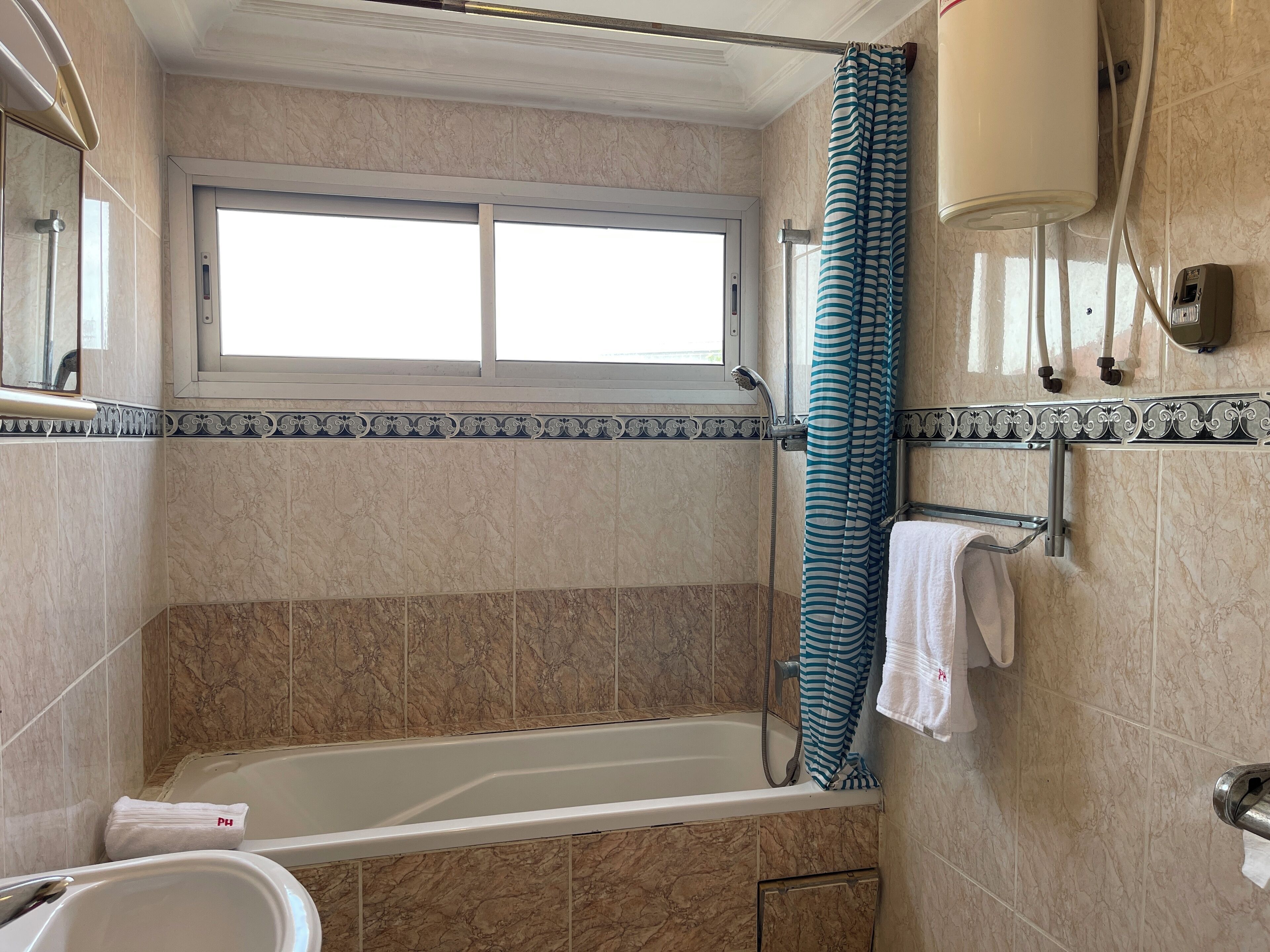 A bathroom with a bathtub, a shower, a window, and a towel rack.