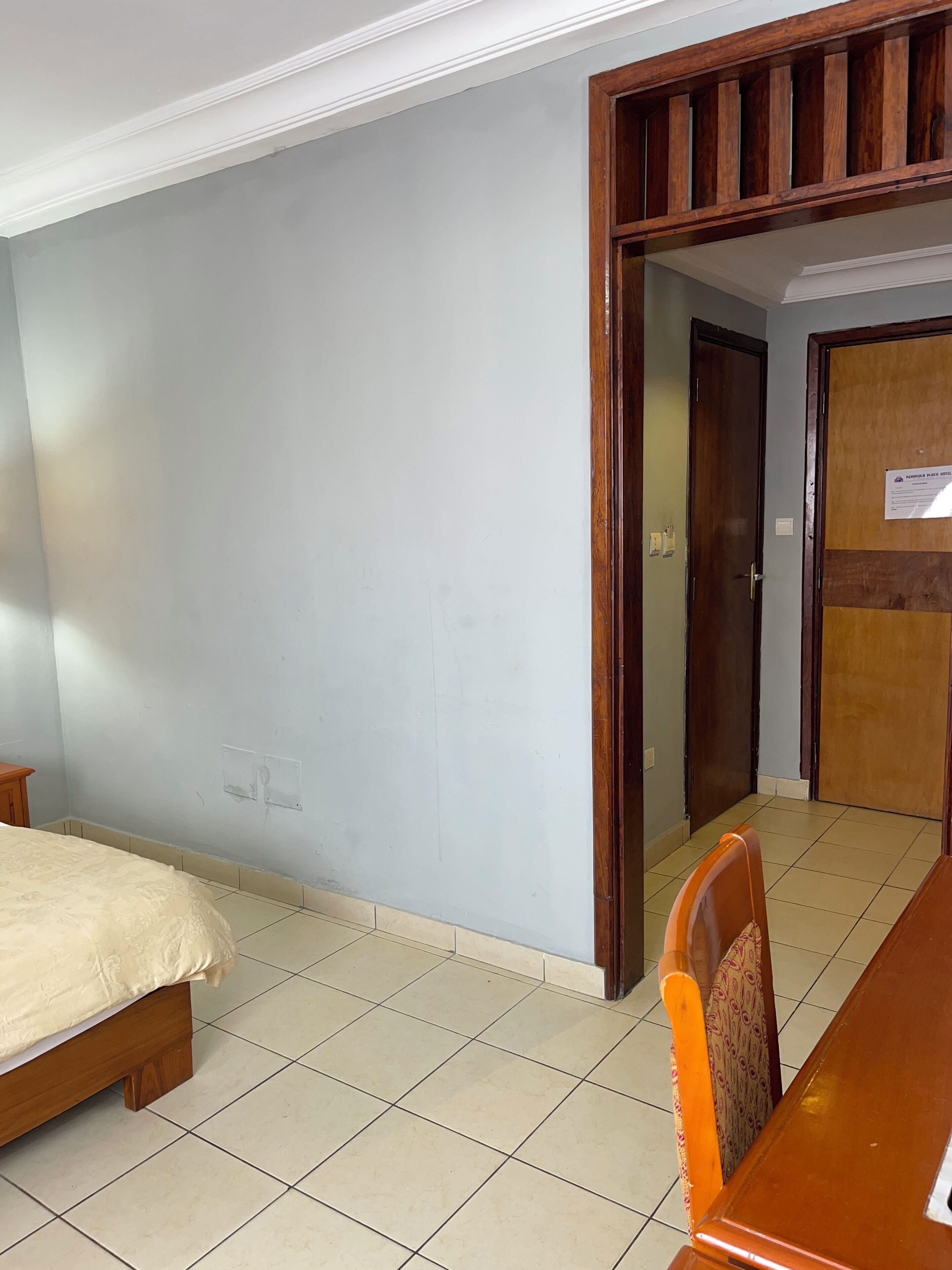 Een kamer met een bed, een houten tafel en een stoel. Er is een deur die naar een andere kamer leidt.
