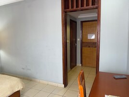 Une chambre d’hôtel avec un lit, une chaise en bois, un bureau et une porte donnant sur une autre pièce.
