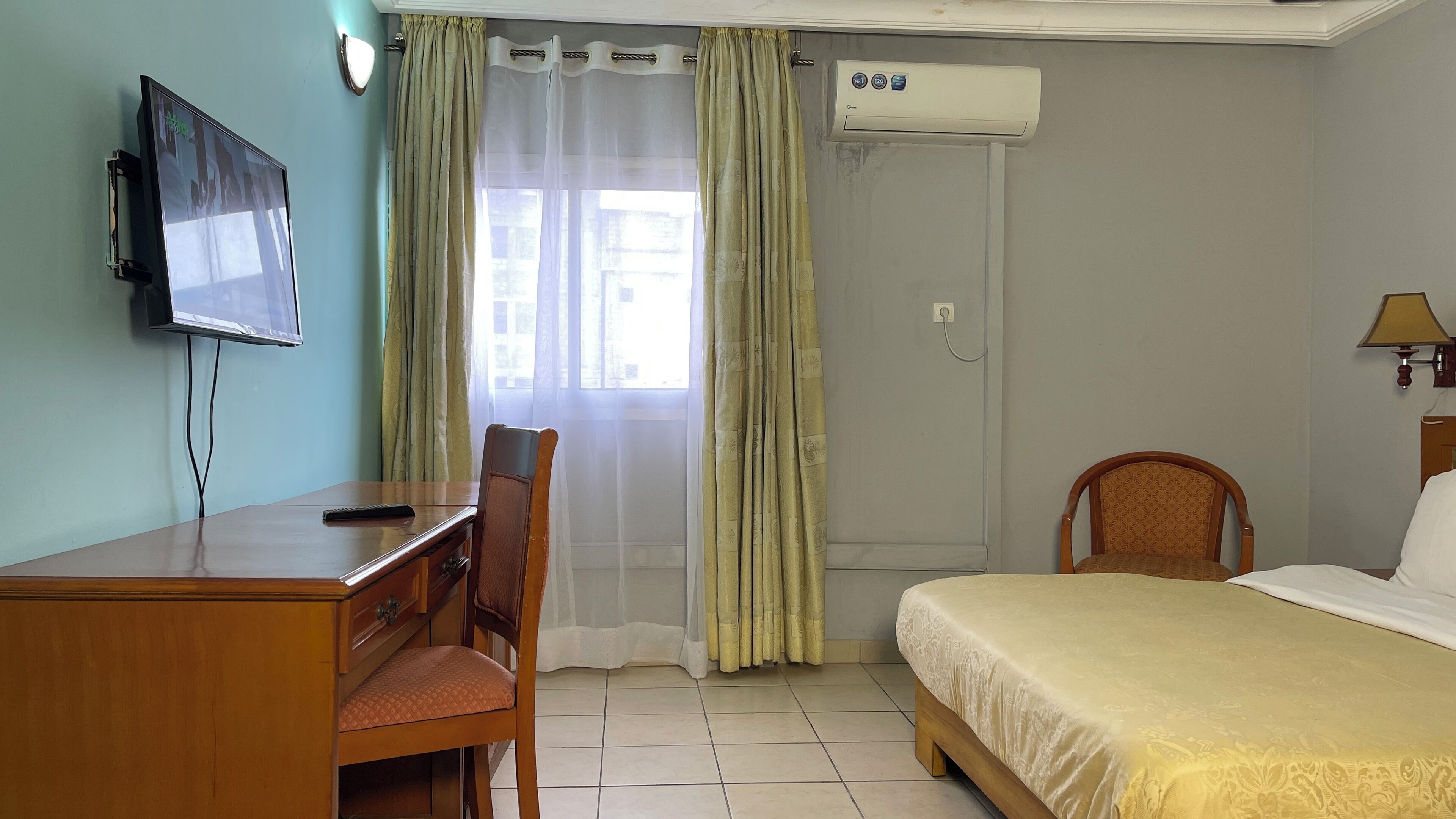 A hotel room with a bed, a desk with a chair, a television, and an air conditioning unit.