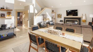 A spacious living room with a fireplace, a dining area with a long table, and a staircase leading to another level. - 3BR Divide Cabin: Starlink, Mtn Views, Hiking Access! Family Friendly - Sleeps 8 (Divide)