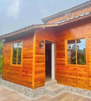 Eine Holzhütte mit zwei Fenstern und einer Tür, einer kleinen Veranda und einem Ziegeldach.
