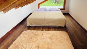 A bedroom with a bed, a large rug, wooden flooring, and a window with a view of greenery. - Lovely cabin with WiFi in charming Circasia (Circasia)