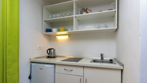 Een kleine keuken met witte kastjes, een spoelbak, een koffiezetapparaat en een afwassigheid.