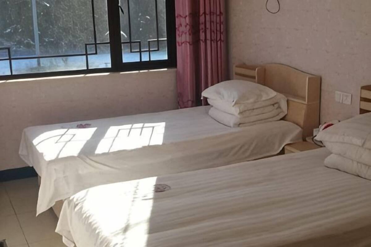 Two single beds with headboards, a window with bars, and a pink curtain.