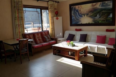 A living room with a sofa, a coffee table, and a dining area with chairs.. Jumanyuan House