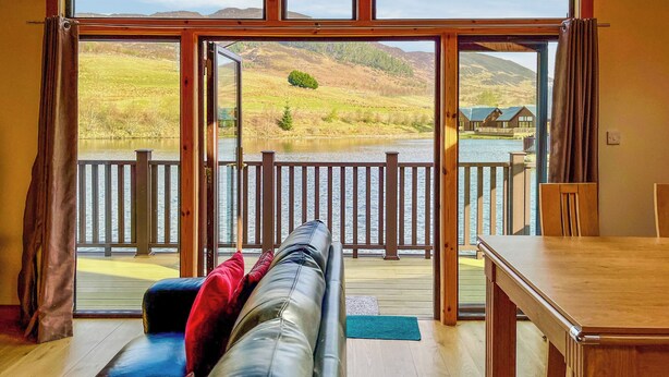 Una habitación con un amplio ventanal que da a una terraza con vistas a un lago y colinas.