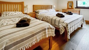 Habitación de hotel con dos camas, cada una con cabecero de madera, mesita de noche, lámpara y ventana con vista a árboles.
