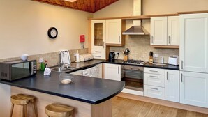 Una cocina moderna con vigas de madera en el techo, un tragaluz, armarios blancos, encimera negra y horno empotrado.