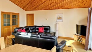 Una sala de estar con un sofá de cuero negro, una mesa de centro de madera y un mueble para televisión.