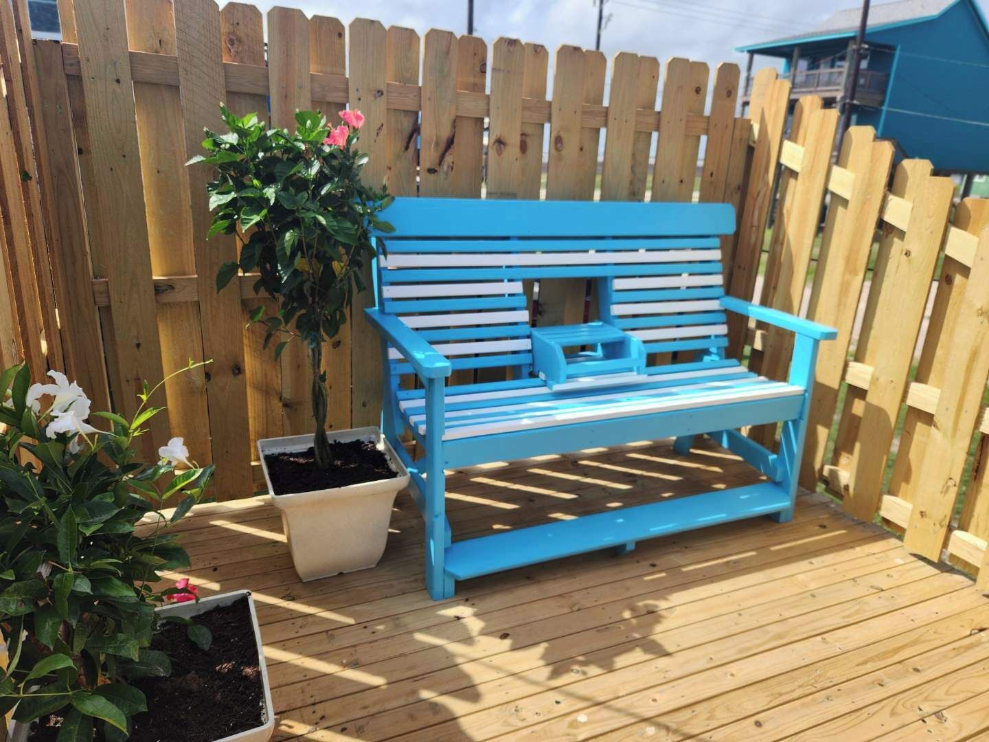 A blue bench with a planter on a wooden deck, surrounded by a wooden fence.