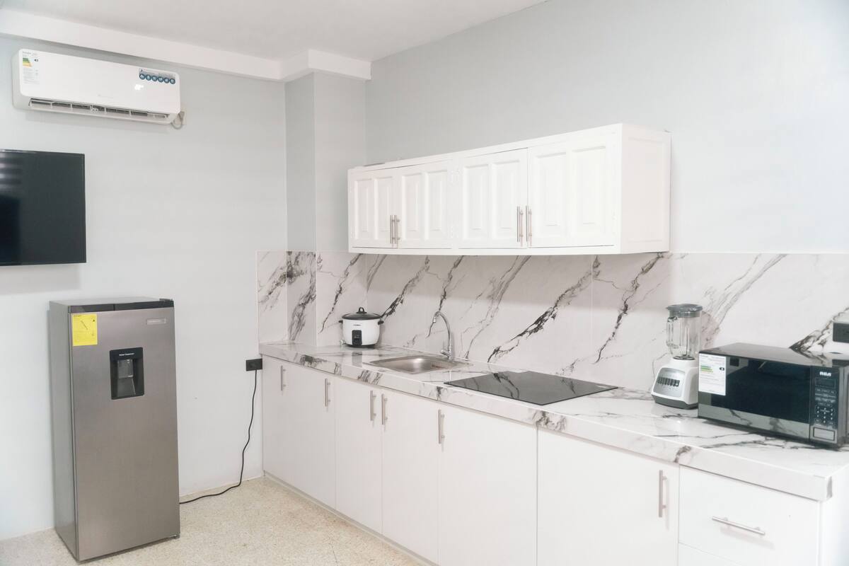 A modern kitchen with white cabinets, a marble backsplash, a built-in microwave, a blender, and a refrigerator.