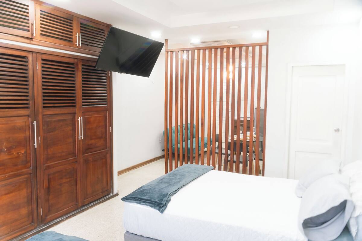 A bedroom with a bed, a TV mounted on the wall, wooden wardrobe, and a sliding door.