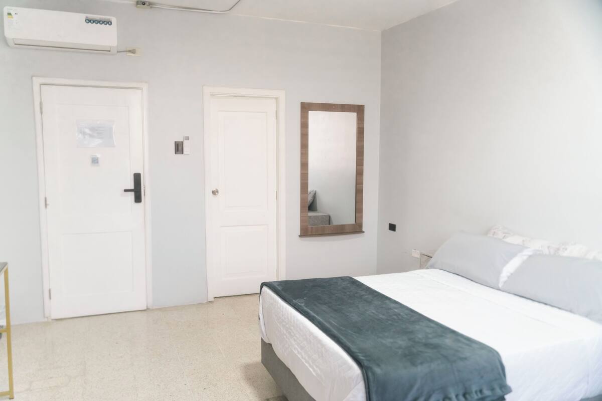 A hotel room with a bed, a mirror, and two white doors.