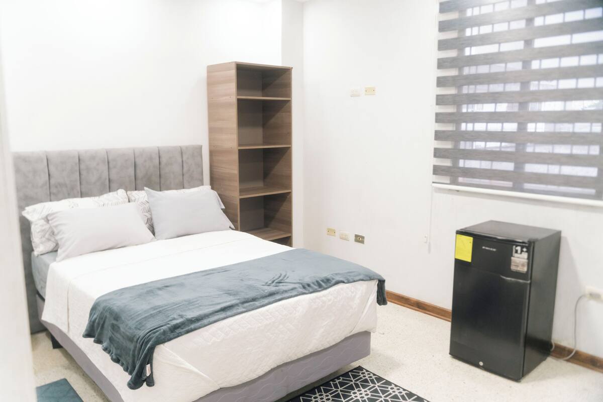 A bedroom with a bed, a wardrobe, a desk, and a window with blinds.