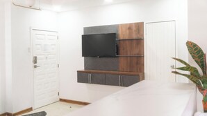 Une chambre à coucher moderne avec un lit, un téléviseur fixé au mur, une porte et une plante en pot.