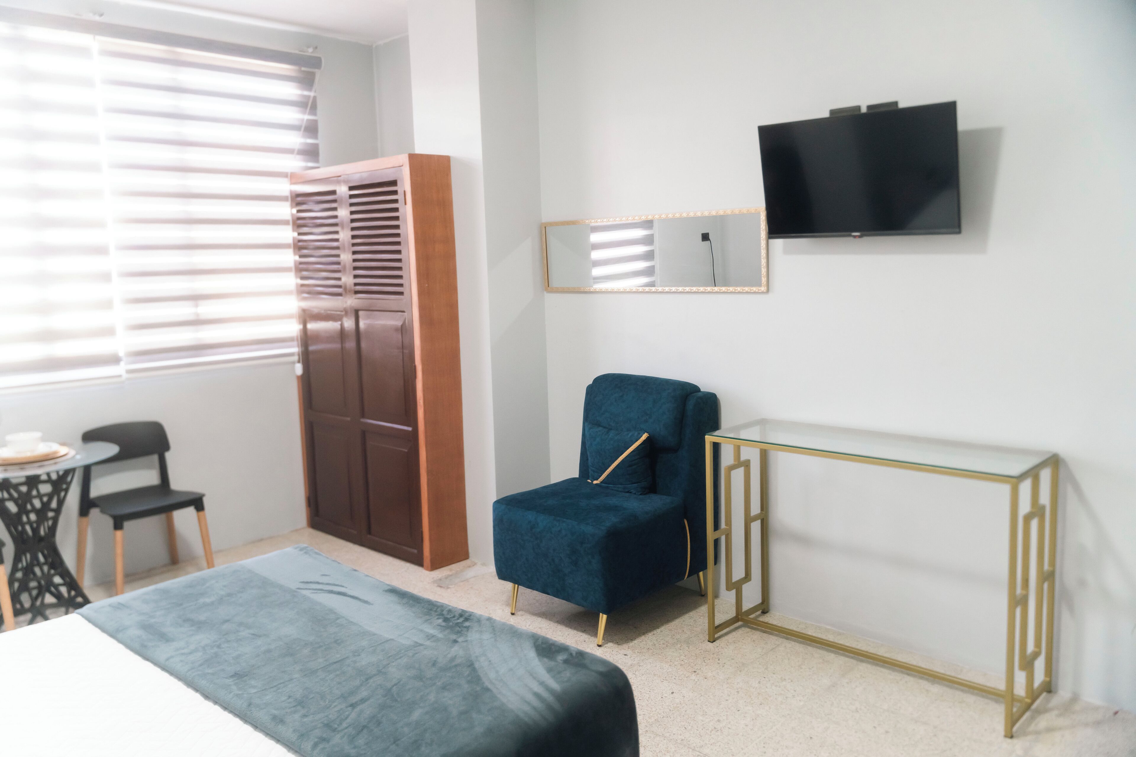 Una habitación con cama, una silla, un armario, una televisión y una mesita.