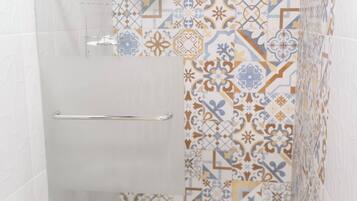 Une douche avec un mur recouvert de carreaux à motifs, une barre d’appui et des toilettes avec un rouleau de papier toilette.