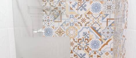 A shower with a patterned tile wall, a grab bar, and a toilet with a roll of toilet paper.
