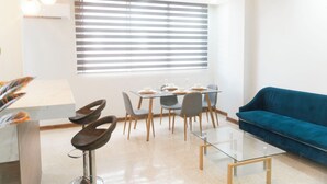 Un salon moderne avec une table basse en verre, un canapé bleu et un coin repas comprenant une table et des chaises en verre.